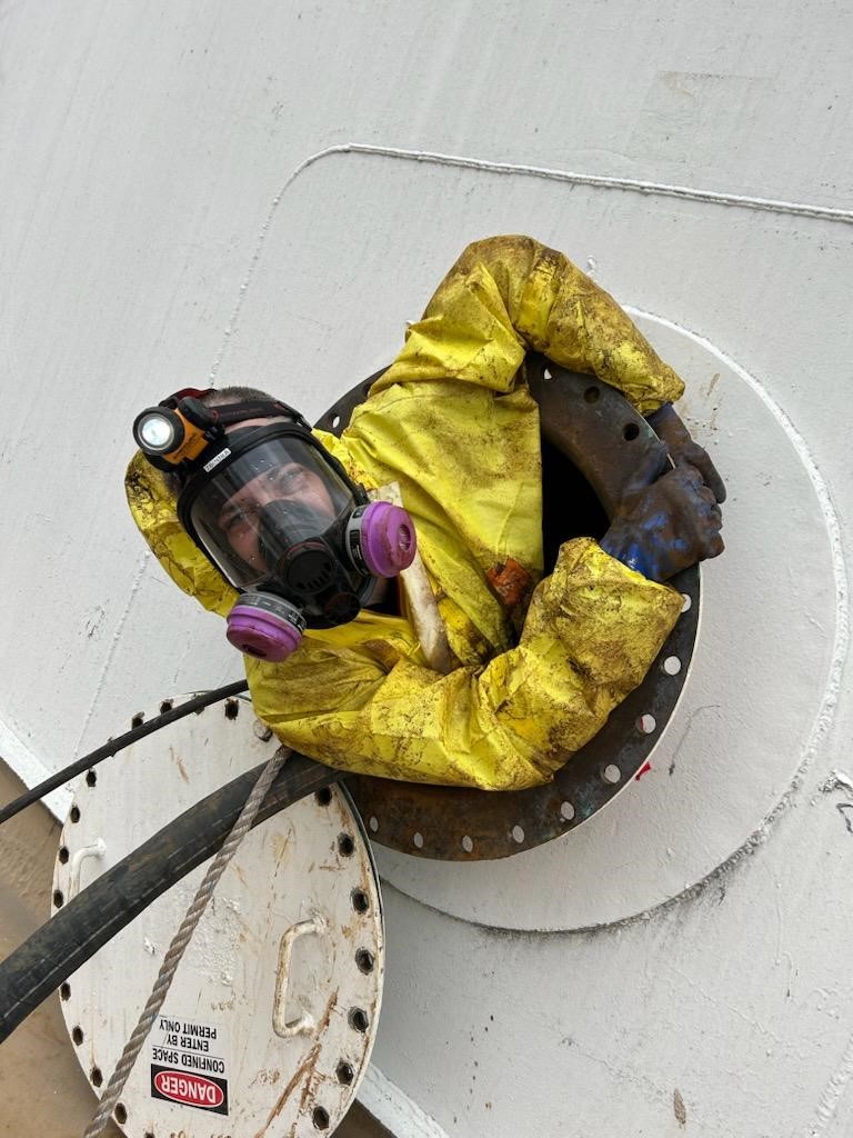 Worker wearing protective gear while emerging from manhole