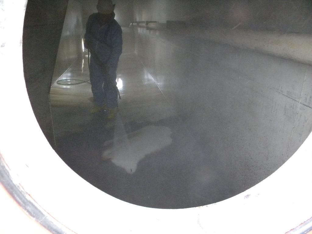 Worker using sprayer to clean floor of storage tank