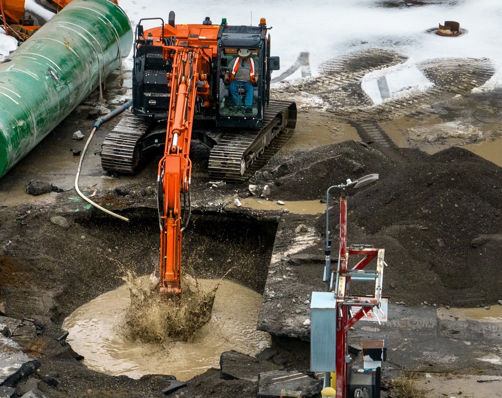 Excavator digging into muddy hole to remove storage tank